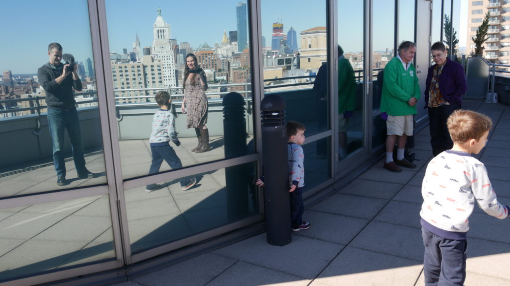 An image of Alexandra and Nathaniel reflected in some large windows as they film their two sons running around in matching shirts. 