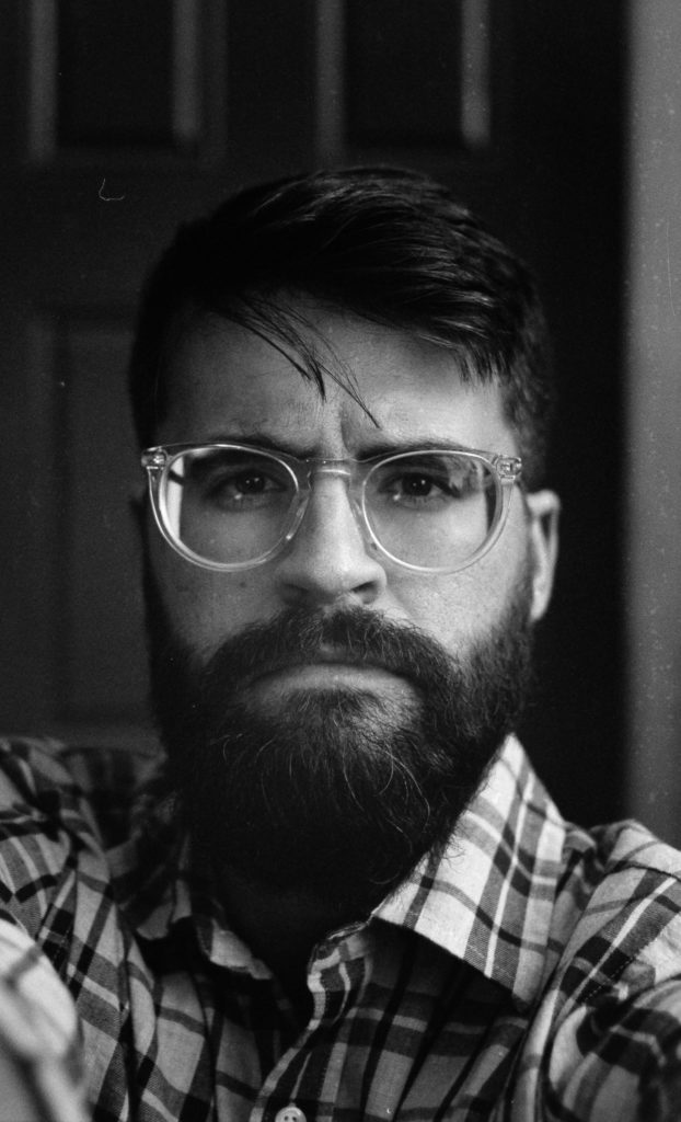 A black-and-white headshot of Johnston, who is looking at the camera with a stoic expression. 